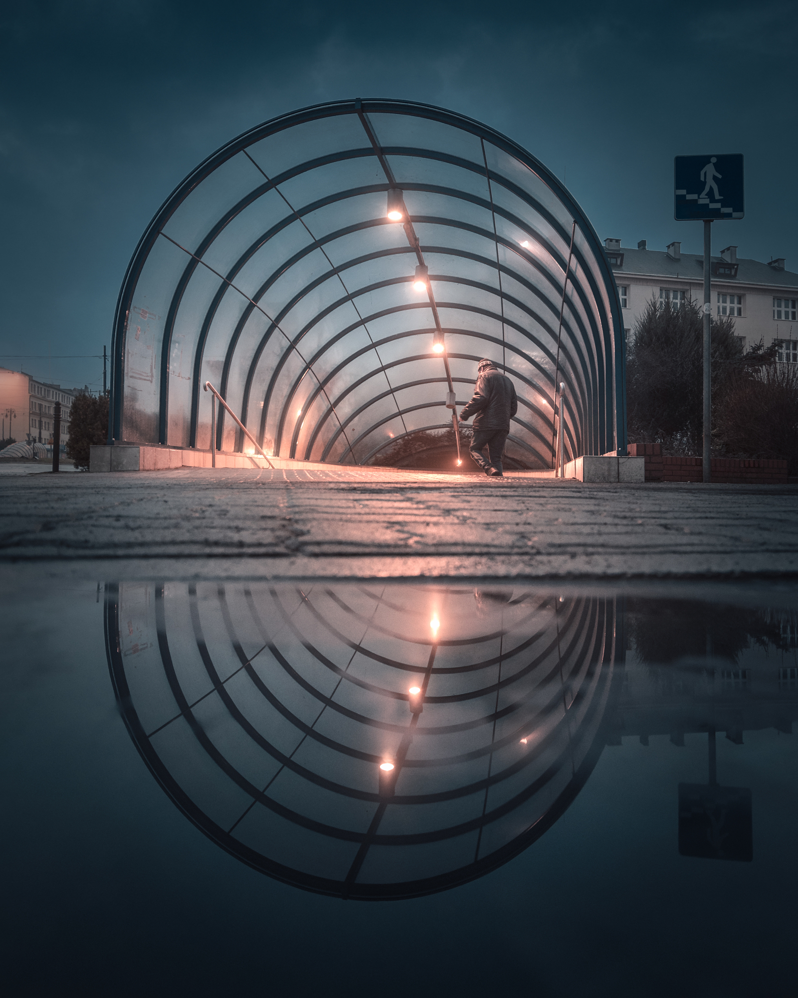 Lit arched tunnel entrance mirrored in a still puddle on a cold blue evening