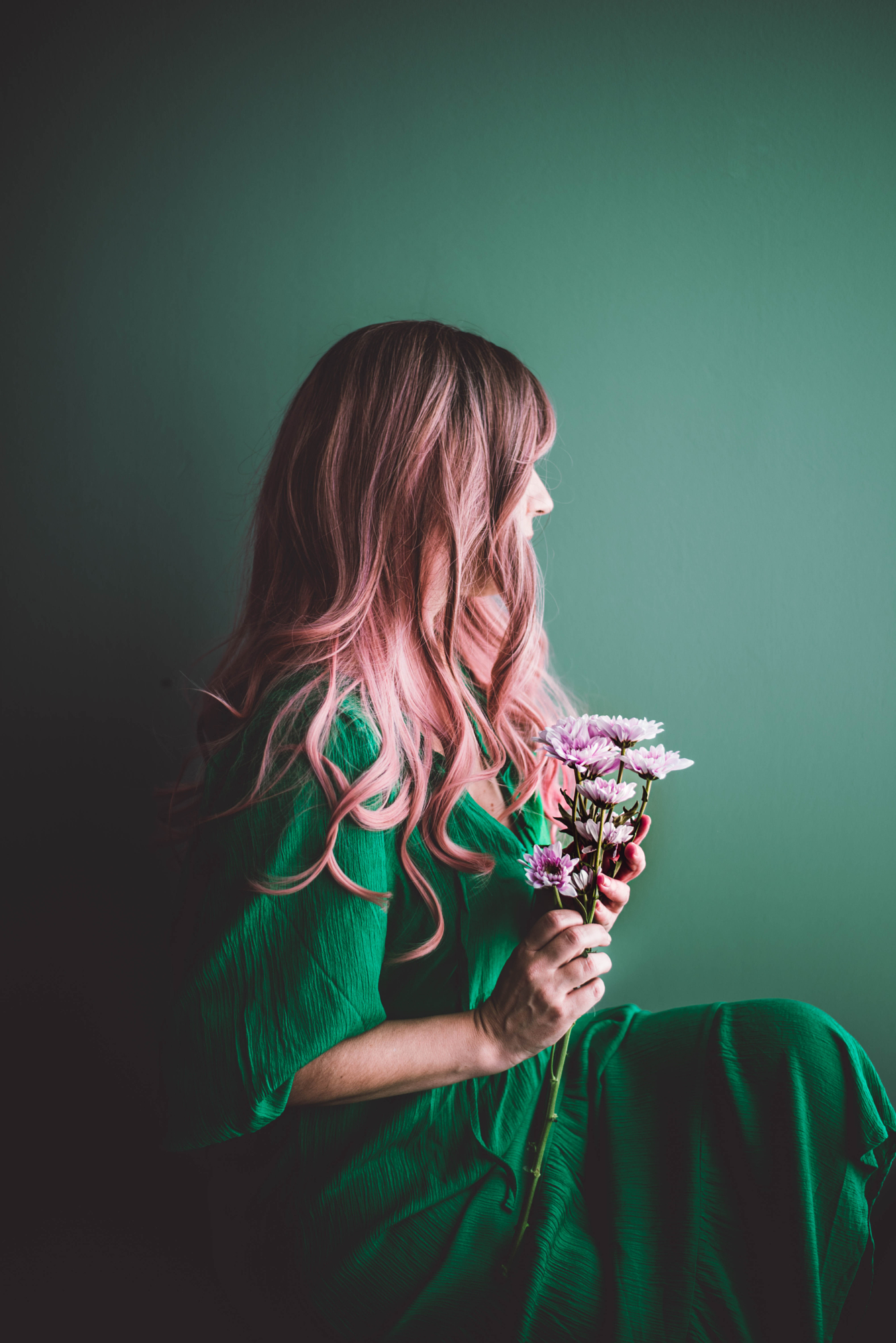 Woman with pink hair in a green dress holding flowers against a green wall, green monochromatic color photography.