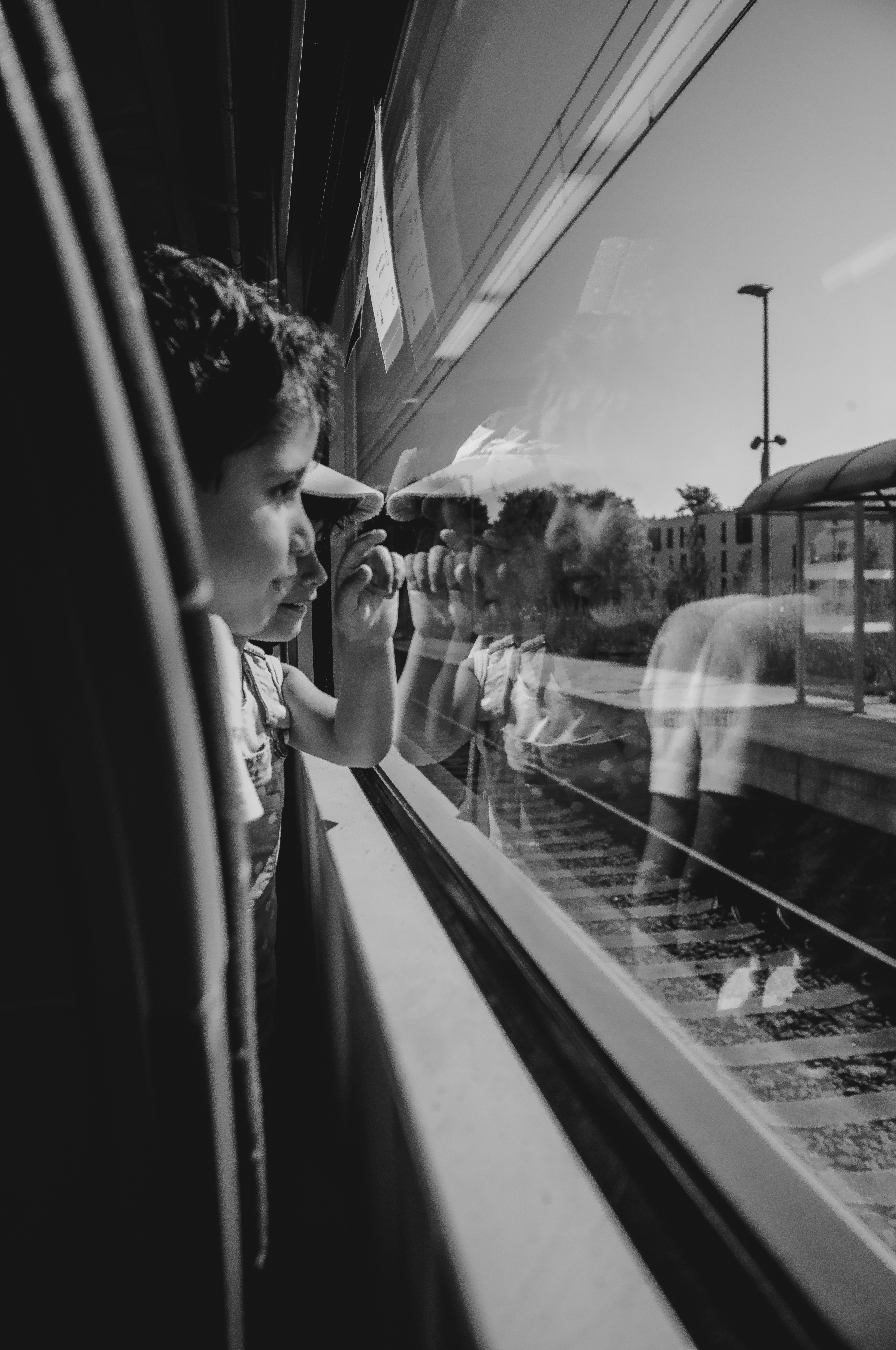 Child leaning out of a train window with their reflection in the glass, from Eline Deckers's street photography.