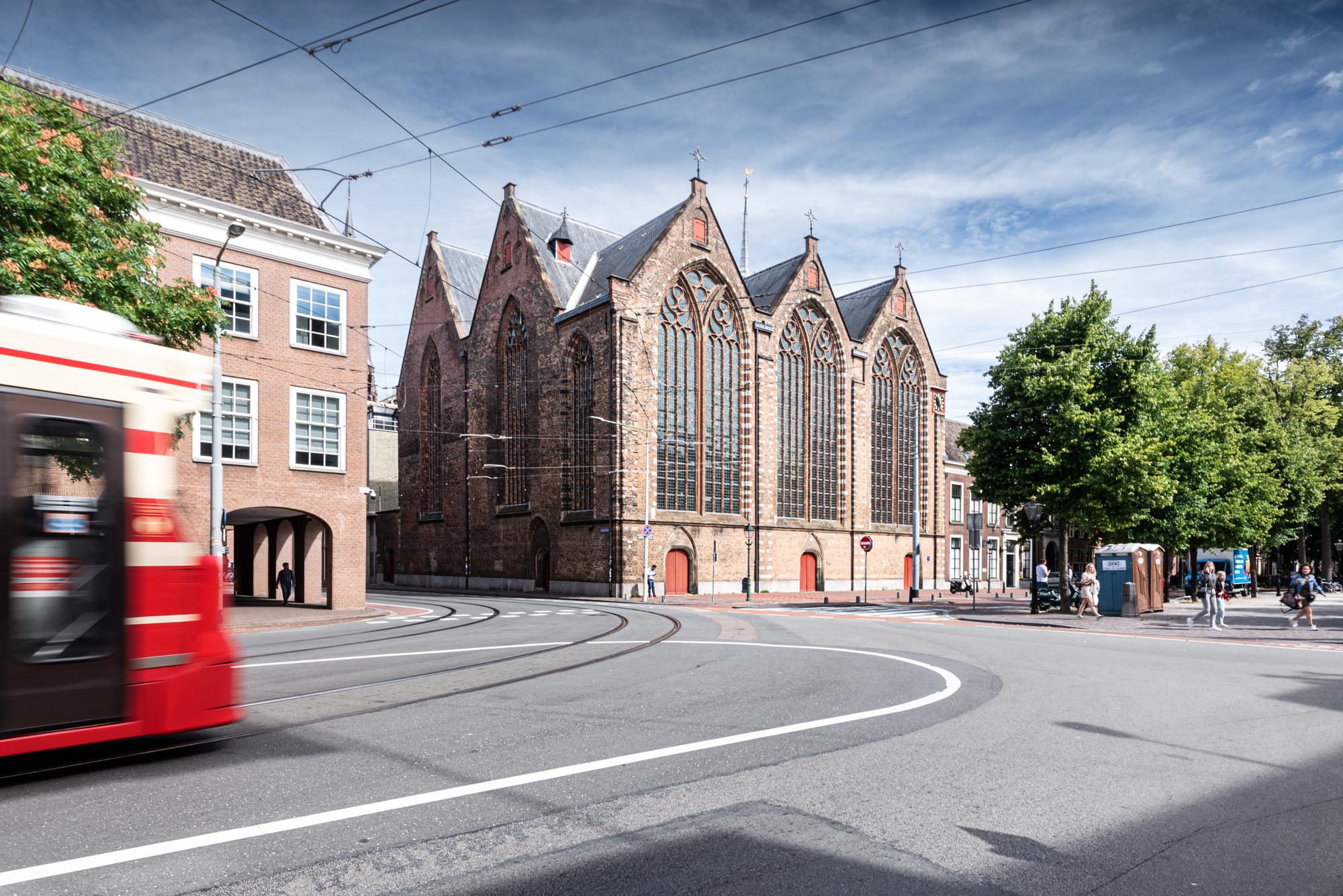 Gothic brick church in The Hague with a red tram blurring past on curved tracks, from Andrew Shenouda's architectural photography.