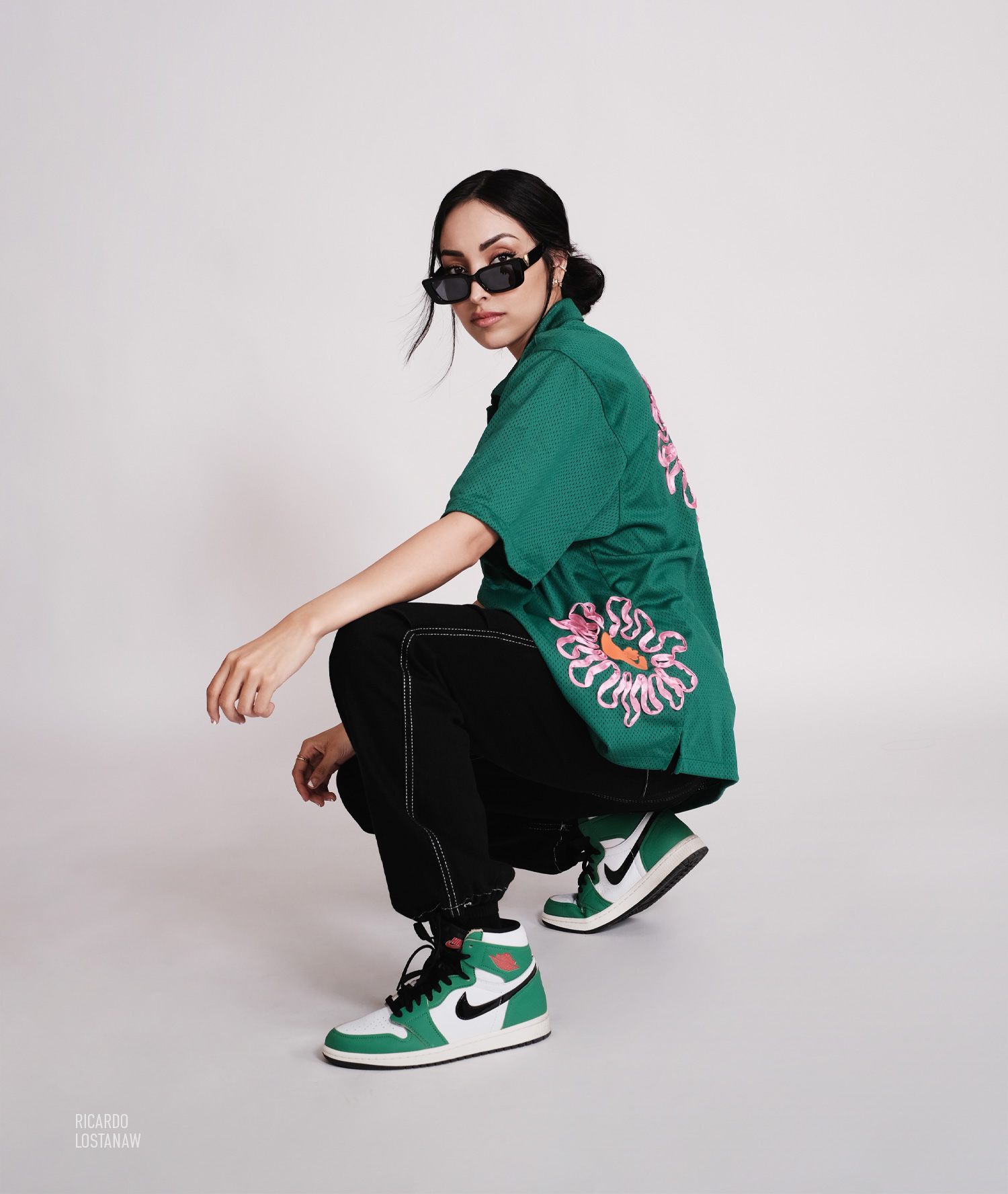 Model crouching in a green mesh jersey and green high-top sneakers on white seamless