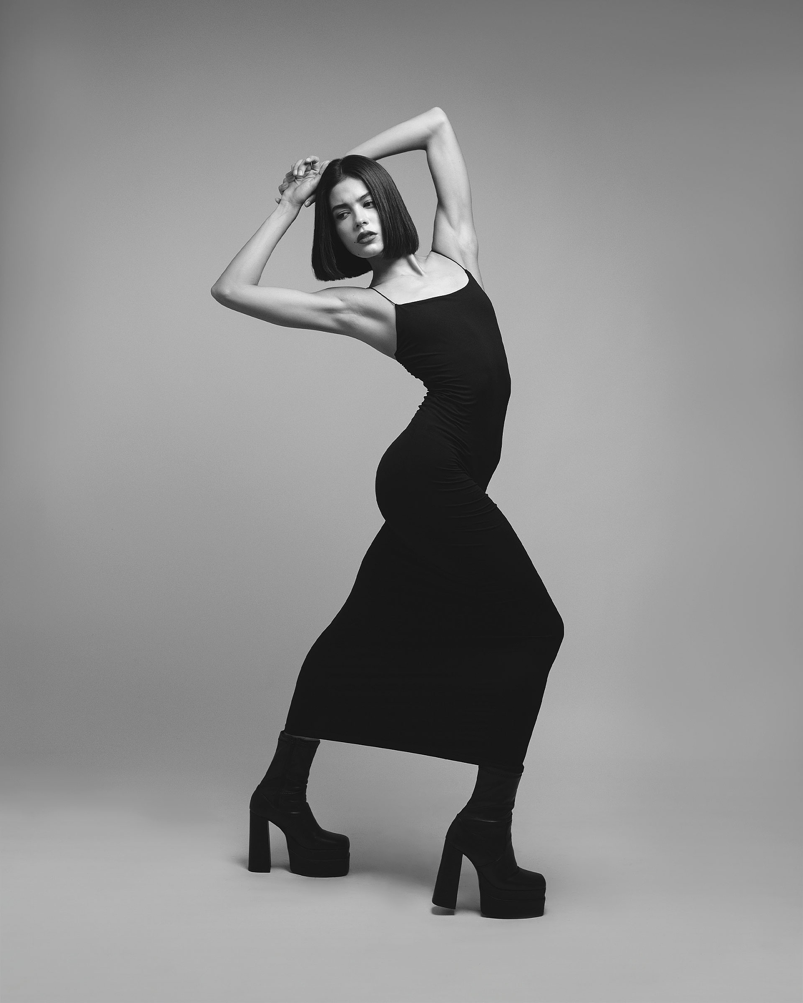Full-length monochrome studio portrait in a long black dress and platform boots