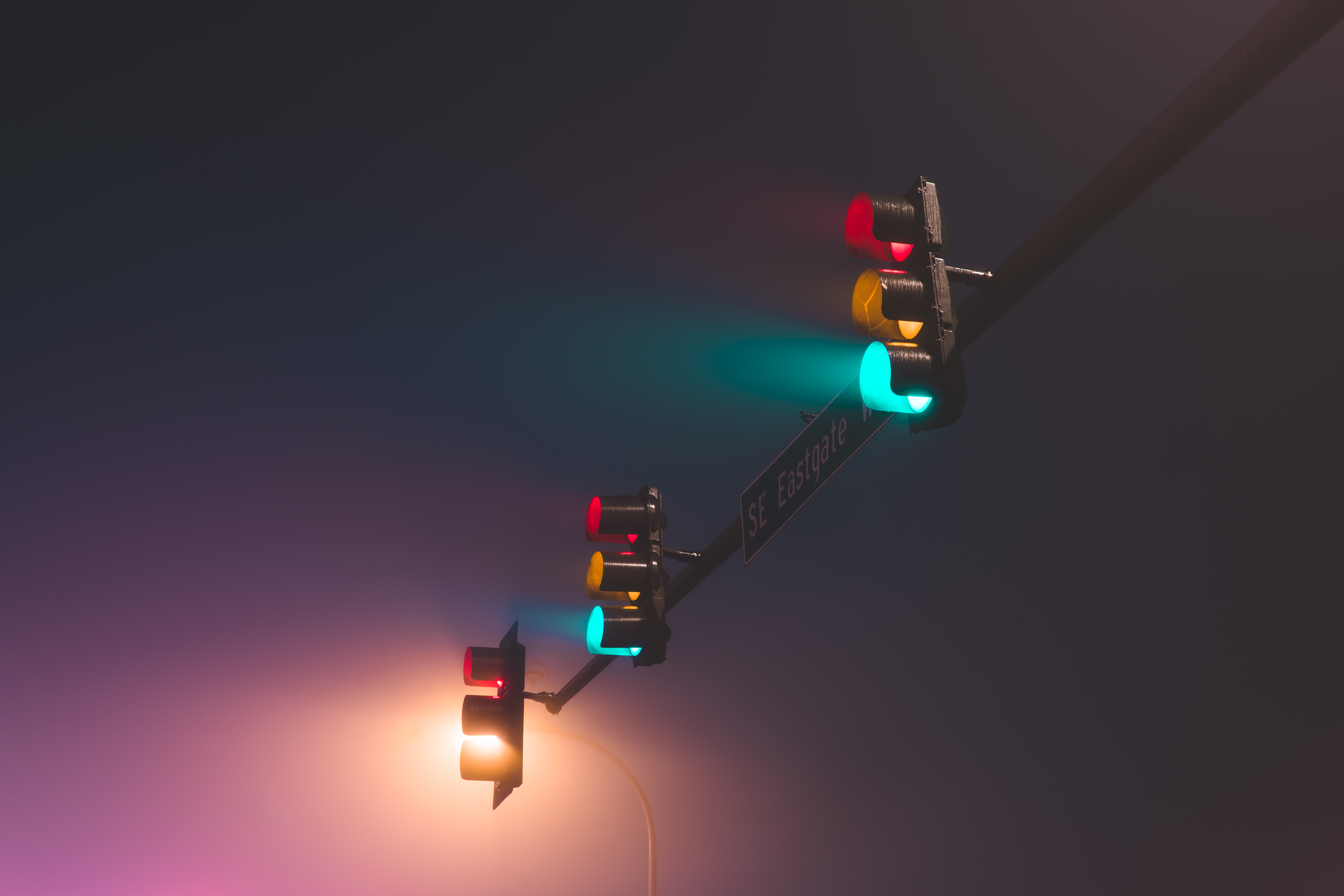 Traffic lights glowing red, amber and teal through dense night fog, an example of urban fog photography with soft halos of light against a hazy purple sky.